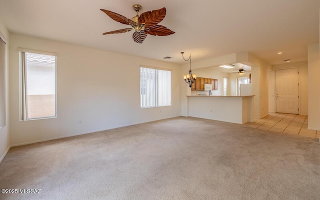 unfurnished living room featuring ceiling fan with notable chandelier, light tile patterned flooring, and light colored carpet