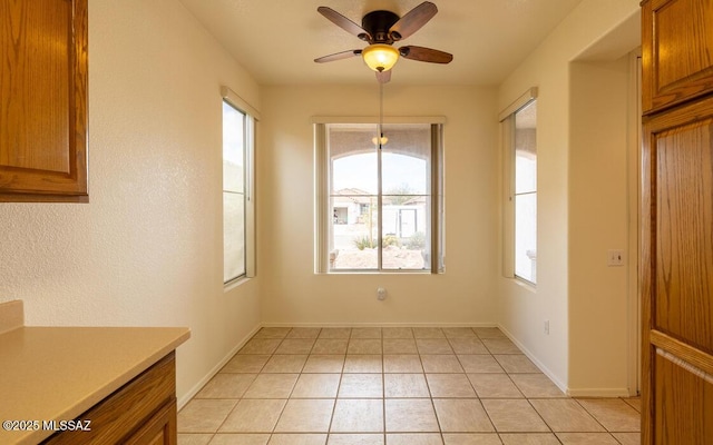 unfurnished dining area featuring light tile patterned floors, baseboards, and a ceiling fan