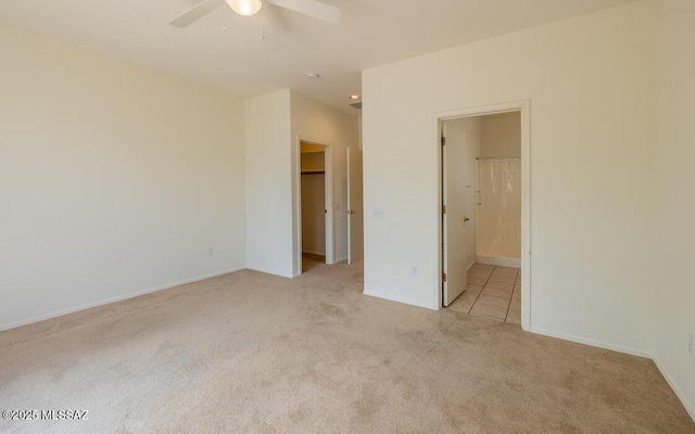 unfurnished bedroom featuring connected bathroom, a walk in closet, light colored carpet, a closet, and a ceiling fan