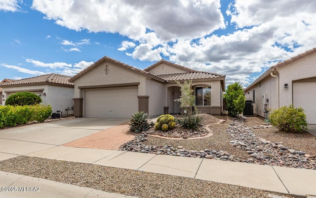 mediterranean / spanish home featuring an attached garage, stucco siding, concrete driveway, a tile roof, and central air condition unit