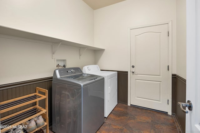 washroom with stone finish floor, wainscoting, laundry area, and washing machine and clothes dryer