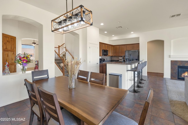 dining room with a tiled fireplace, visible vents, arched walkways, and stairs