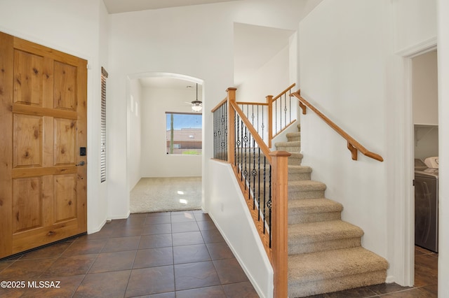 foyer entrance with arched walkways, ceiling fan, stairs, dark tile patterned floors, and washing machine and dryer