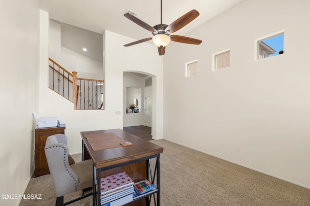 home office with visible vents, carpet floors, arched walkways, ceiling fan, and a towering ceiling