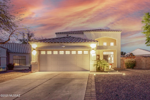 mediterranean / spanish-style home featuring fence, a tiled roof, a garage, concrete driveway, and stucco siding