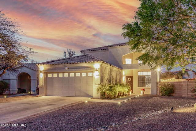 mediterranean / spanish house with stucco siding, a tile roof, a garage, and concrete driveway