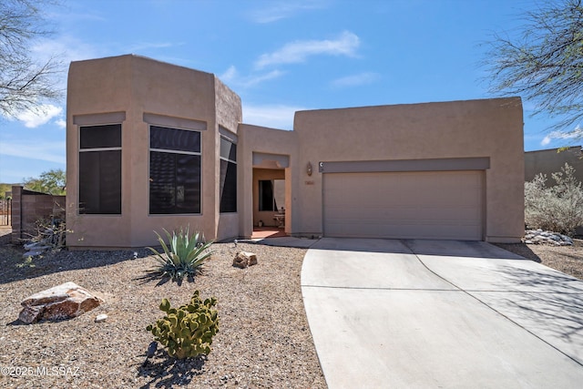 pueblo revival-style home featuring a garage, driveway, and stucco siding