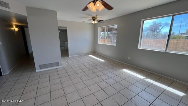 empty room with light tile patterned flooring, baseboards, ceiling fan, and visible vents
