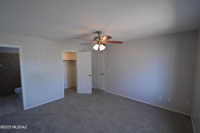 unfurnished bedroom featuring connected bathroom, a walk in closet, carpet floors, a textured ceiling, and a ceiling fan