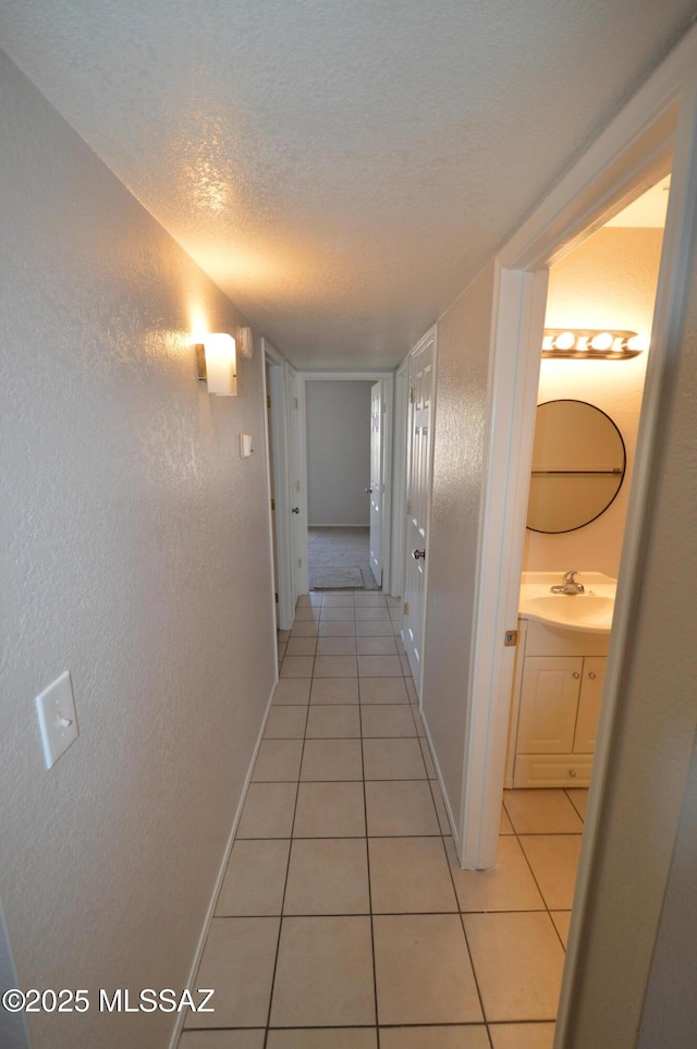 corridor with a textured wall, a textured ceiling, a sink, and light tile patterned floors