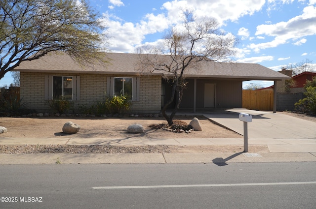 ranch-style home with fence, roof with shingles, concrete driveway, an attached carport, and brick siding