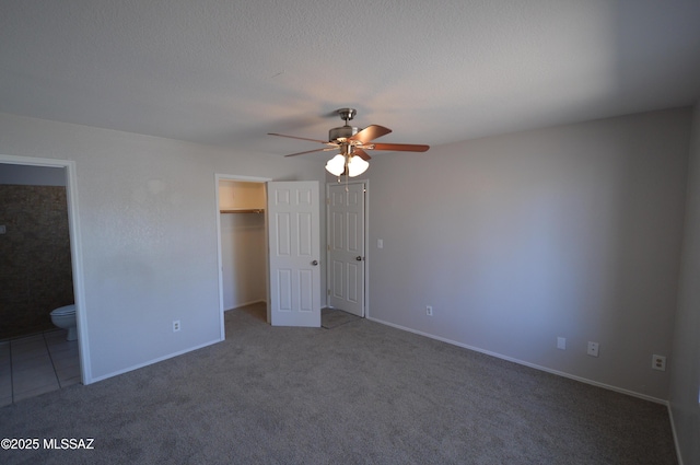unfurnished bedroom featuring a textured ceiling, connected bathroom, a ceiling fan, carpet floors, and a spacious closet
