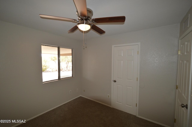 empty room featuring dark carpet, a ceiling fan, and baseboards