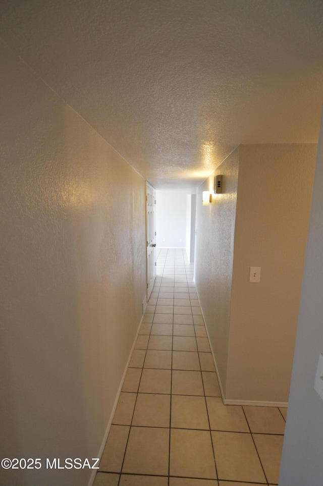 hall with light tile patterned floors, a textured wall, baseboards, and a textured ceiling