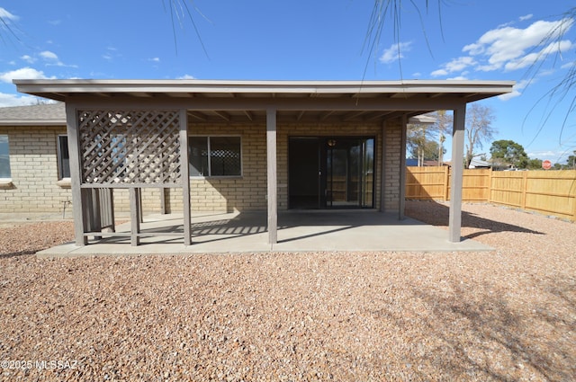 back of house featuring fence, brick siding, and a patio