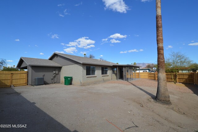 back of house with central AC unit, a fenced backyard, and brick siding