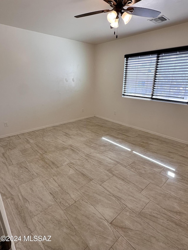 empty room featuring visible vents, a ceiling fan, and baseboards