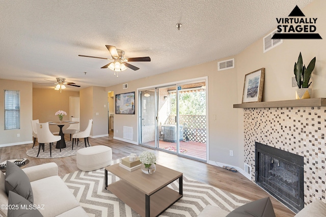 living room with visible vents, a textured ceiling, a fireplace, and light wood finished floors