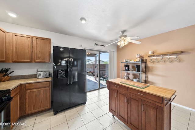 kitchen featuring butcher block counters, light tile patterned floors, brown cabinetry, black appliances, and a ceiling fan