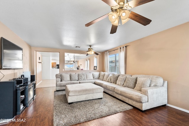 living room featuring ceiling fan with notable chandelier, visible vents, baseboards, and dark wood-style flooring