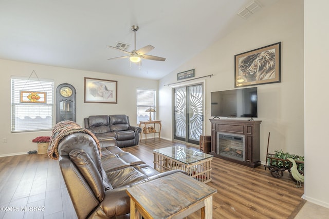 living area featuring visible vents, wood finished floors, a glass covered fireplace, lofted ceiling, and ceiling fan