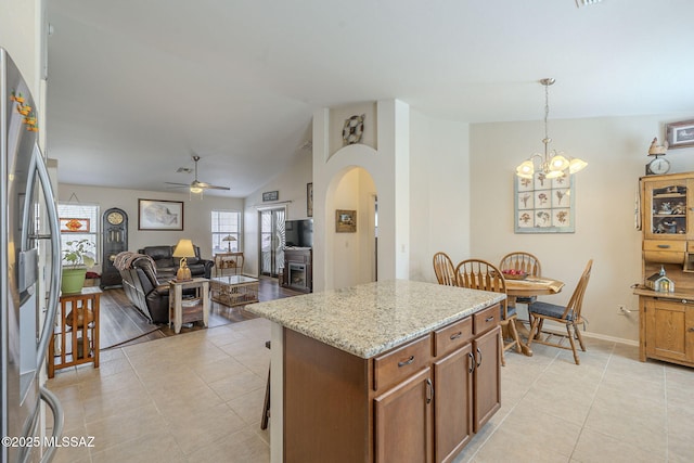 kitchen featuring stainless steel refrigerator with ice dispenser, open floor plan, arched walkways, brown cabinetry, and lofted ceiling