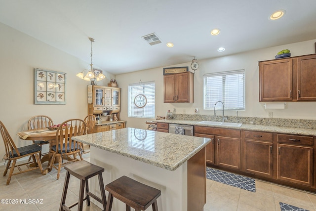 kitchen featuring visible vents, a kitchen island, dishwasher, a breakfast bar, and a sink