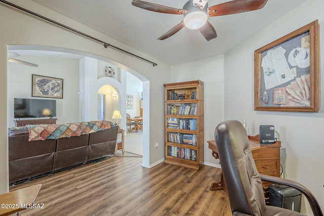 office with wood finished floors, baseboards, arched walkways, and ceiling fan