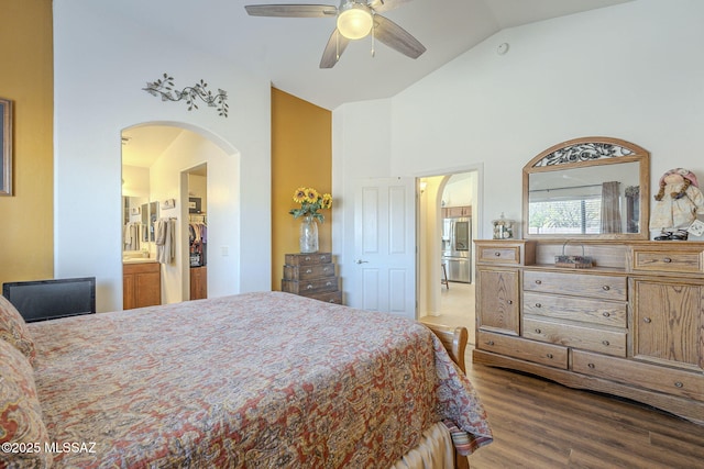 bedroom with a ceiling fan, wood finished floors, high vaulted ceiling, stainless steel fridge, and connected bathroom