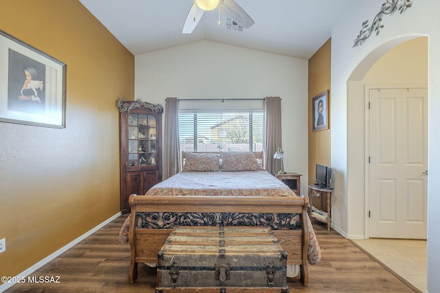 bedroom featuring a ceiling fan, wood finished floors, visible vents, arched walkways, and vaulted ceiling