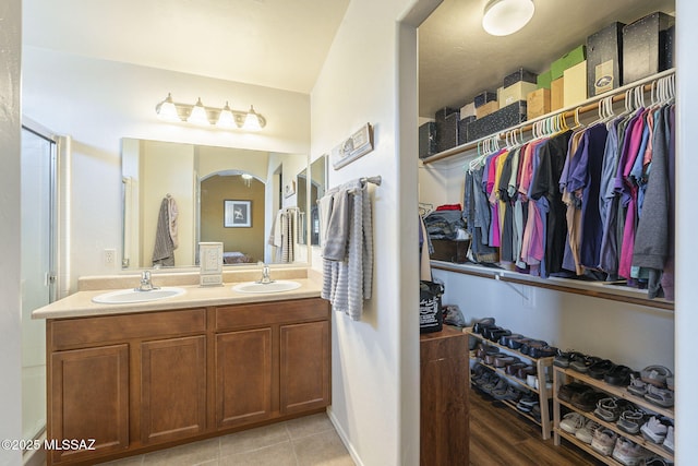 full bathroom featuring double vanity, tile patterned floors, a walk in closet, and a sink