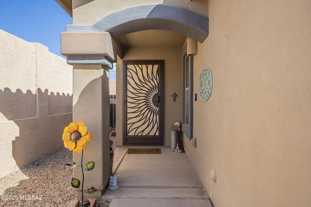 view of exterior entry featuring stucco siding and fence