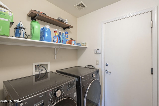 clothes washing area with visible vents, washer and dryer, and laundry area