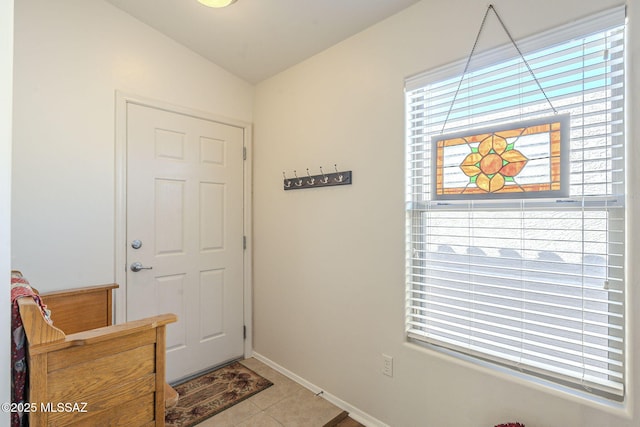 entryway featuring baseboards, a healthy amount of sunlight, tile patterned flooring, and vaulted ceiling