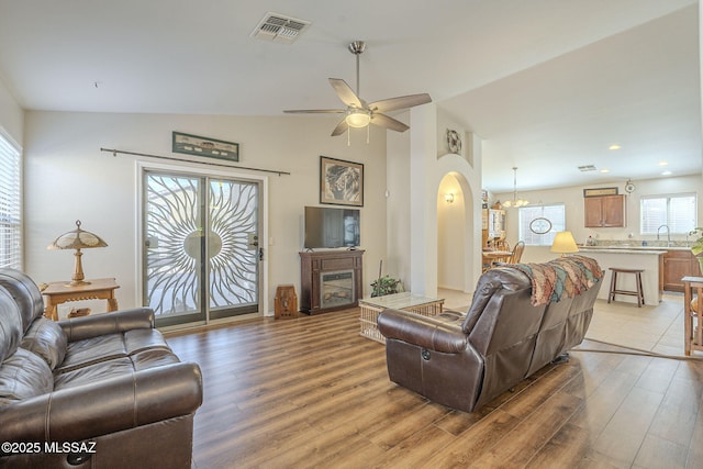 living room with light wood-type flooring, visible vents, arched walkways, and vaulted ceiling