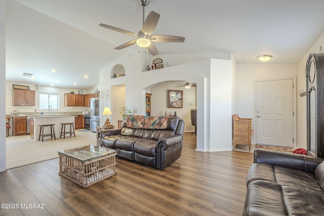 living area featuring baseboards, ceiling fan, light wood-type flooring, lofted ceiling, and arched walkways