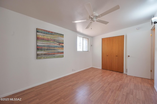 unfurnished bedroom with baseboards, vaulted ceiling, light wood-style flooring, a closet, and a ceiling fan