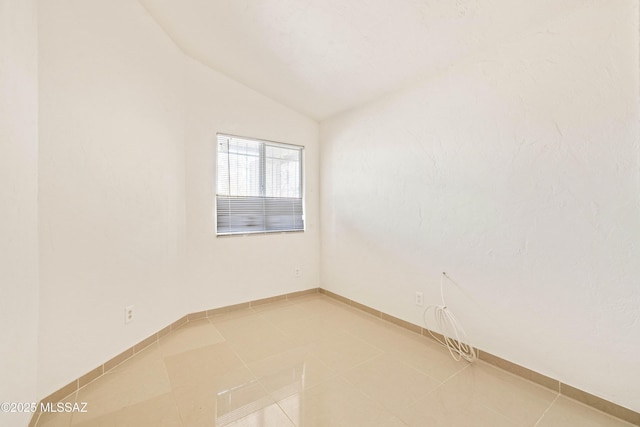 empty room featuring light tile patterned floors, baseboards, and lofted ceiling