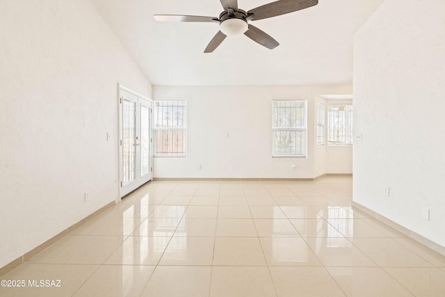 empty room featuring vaulted ceiling, light tile patterned flooring, a ceiling fan, and baseboards