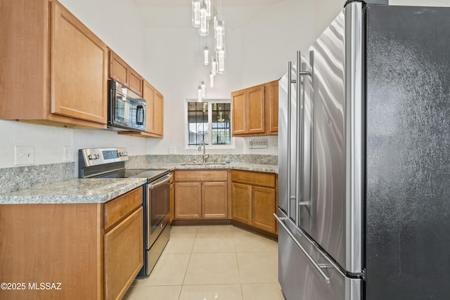 kitchen featuring light tile patterned flooring, brown cabinetry, appliances with stainless steel finishes, and a sink