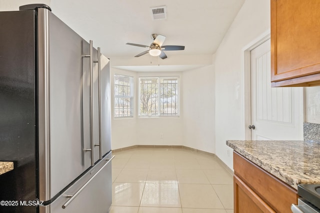 kitchen featuring light tile patterned floors, brown cabinetry, visible vents, freestanding refrigerator, and ceiling fan