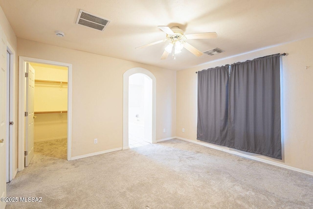 carpeted empty room featuring visible vents, arched walkways, baseboards, and a ceiling fan