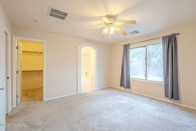 unfurnished bedroom with arched walkways, visible vents, light colored carpet, and a walk in closet