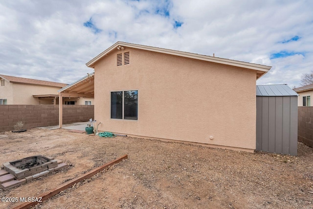 back of property featuring a patio, an outdoor structure, a fenced backyard, and an outdoor fire pit