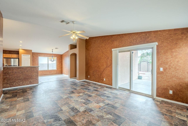 unfurnished living room featuring arched walkways, ceiling fan with notable chandelier, stone finish flooring, and baseboards