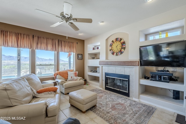 tiled living room with a fireplace, built in features, and ceiling fan