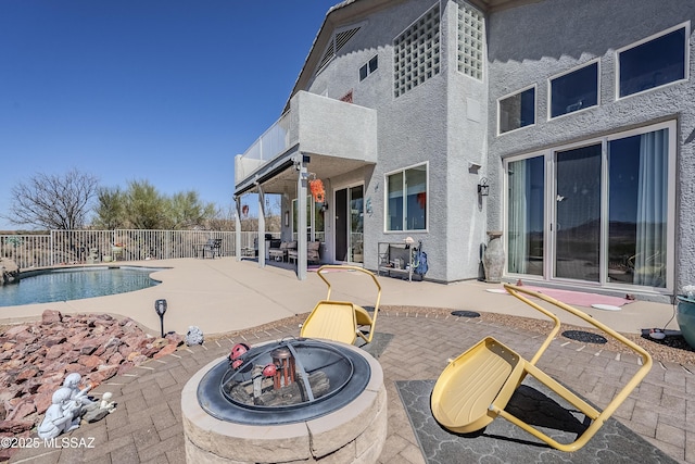 view of patio with a fire pit, a fenced in pool, fence, and a balcony