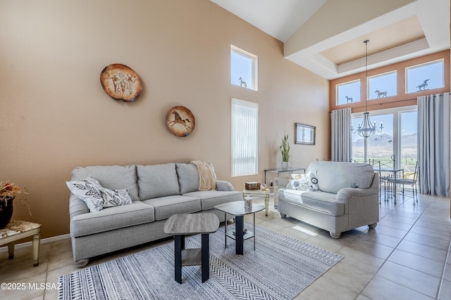 living room featuring a towering ceiling, a notable chandelier, a tray ceiling, and light tile patterned flooring