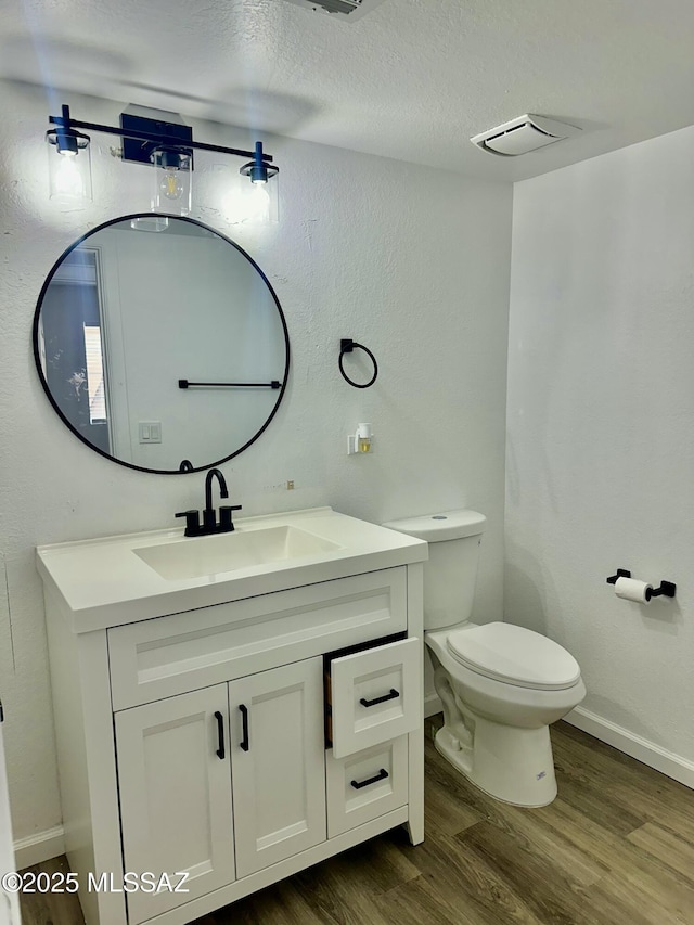 bathroom with visible vents, toilet, a textured ceiling, wood finished floors, and vanity