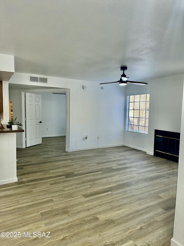 unfurnished living room with visible vents, a textured ceiling, a ceiling fan, and wood finished floors